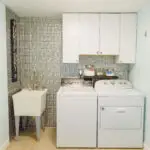 Laundry room remodel with white washer dryer, upper cabinets, utility sink, and green mosaic tile accent wall