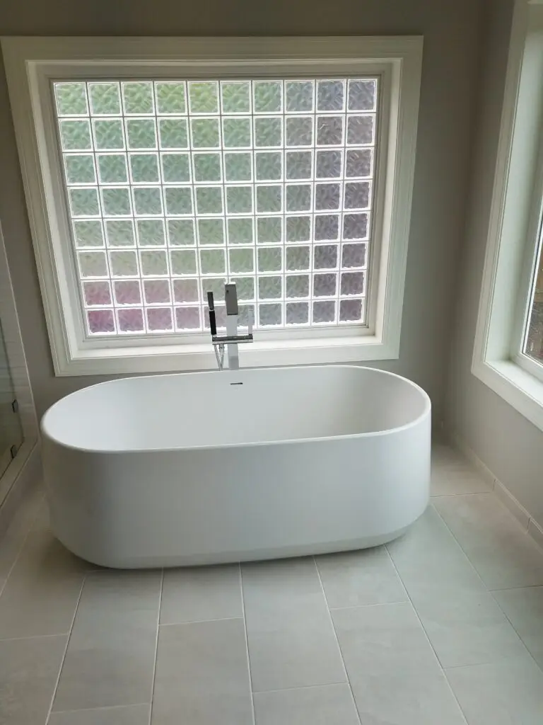 Freestanding soaking tub set below a glass block window