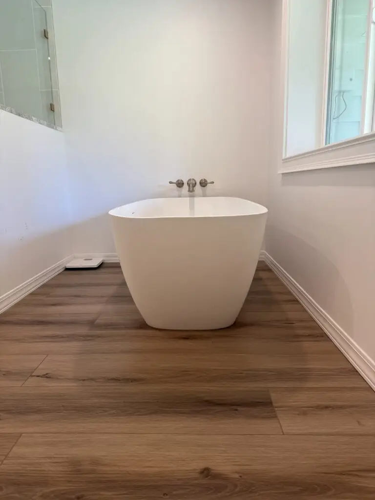 Freestanding white soaking tub with a wall-mounted filler and wood-look plank flooring in a remodeled Camas, WA master bathroom
