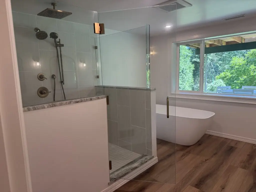 Walk-in tile shower with a frameless glass enclosure and granite-capped half wall in a remodeled Camas, WA master bathroom