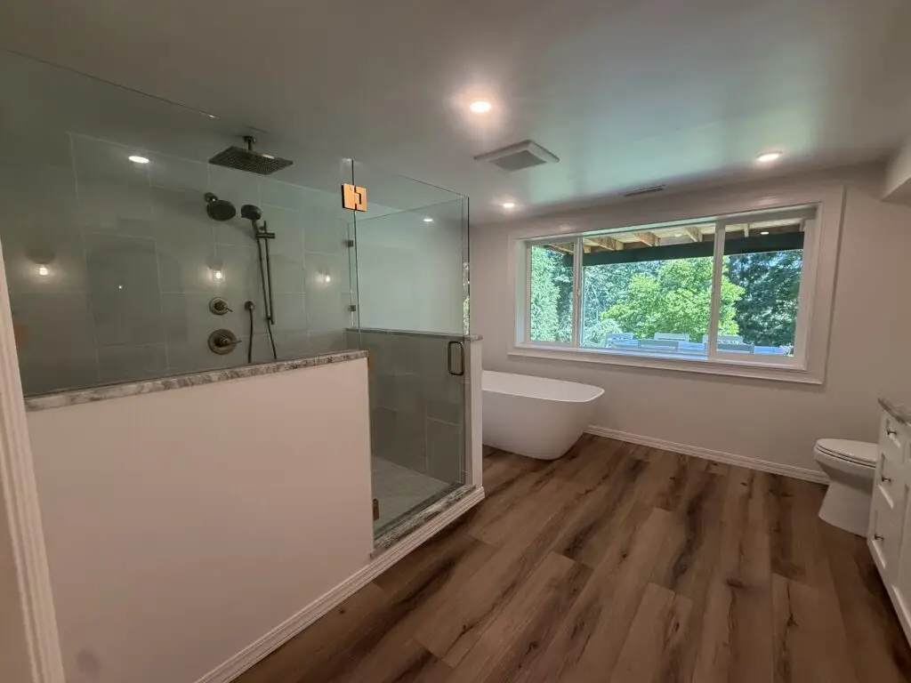 Completed master bathroom remodel in Camas, WA with a walk-in glass shower, freestanding soaking tub and wood-look plank flooring by TLC Home Solutions