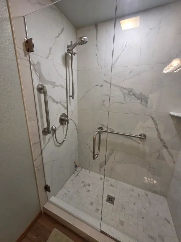 Walk-in shower with marble-look tile walls, a mosaic tile floor, grab bars and a glass door in a remodeled Vancouver, WA bathroom