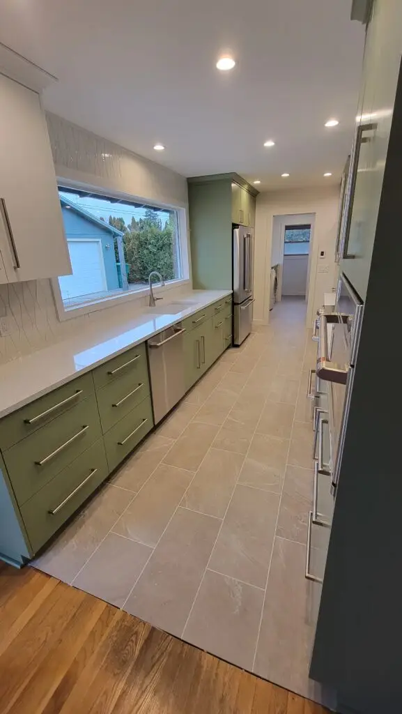 Remodeled galley kitchen with olive green cabinets, a geometric tile backsplash and a wide window over the counter in Vancouver, WA