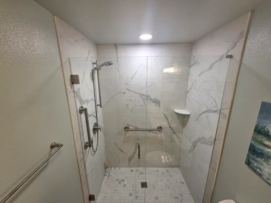 Accessible walk-in shower with grab bars, a hand shower on a slide bar and marble-look tile in a remodeled Vancouver, WA bathroom