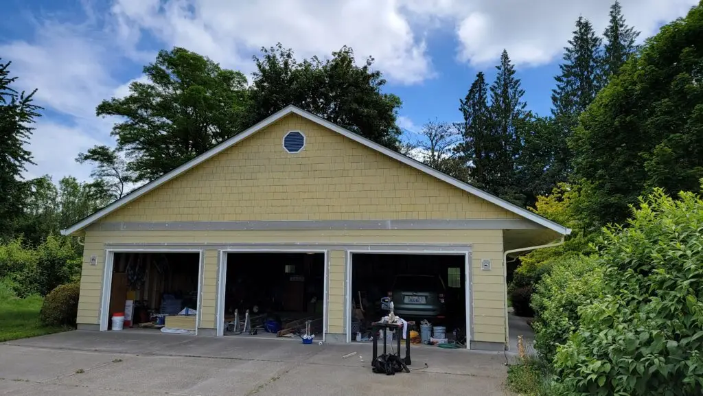 Detached three-car garage with yellow siding being prepped and repainted during an exterior project