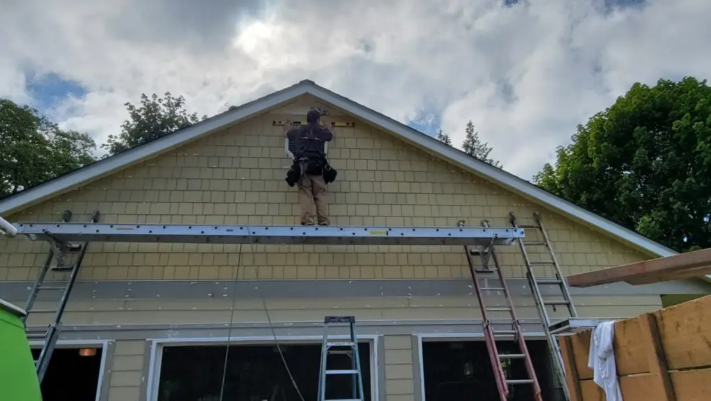 TLC Home Solutions crew member replacing siding at a gable end from a ladder during an exterior project